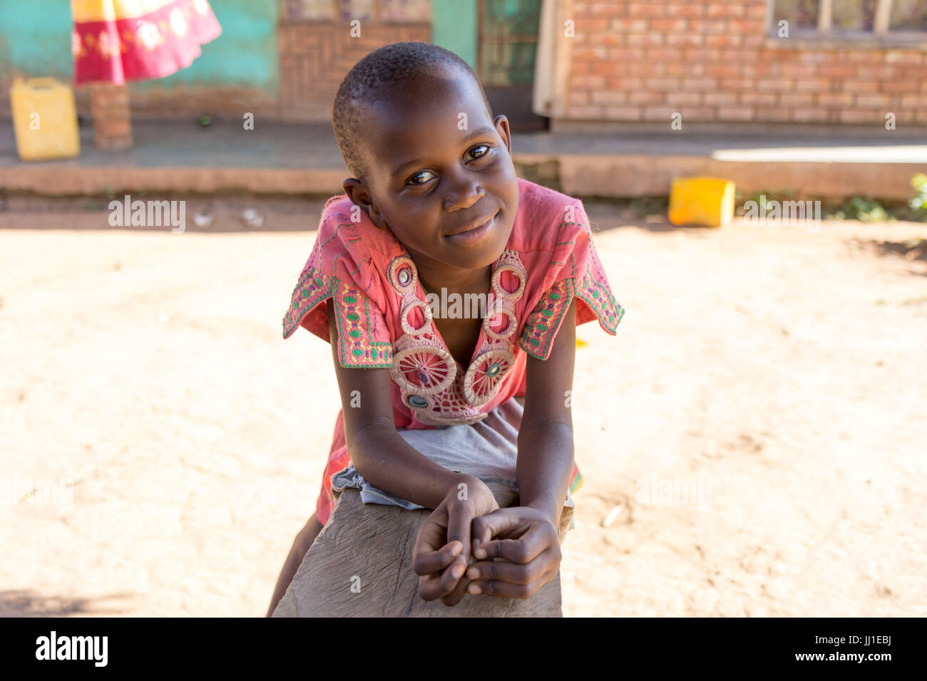 Un enfant de 9 ans smiling ougandaise appuyée sur un banc et regardant la caméra Banque D'Images
