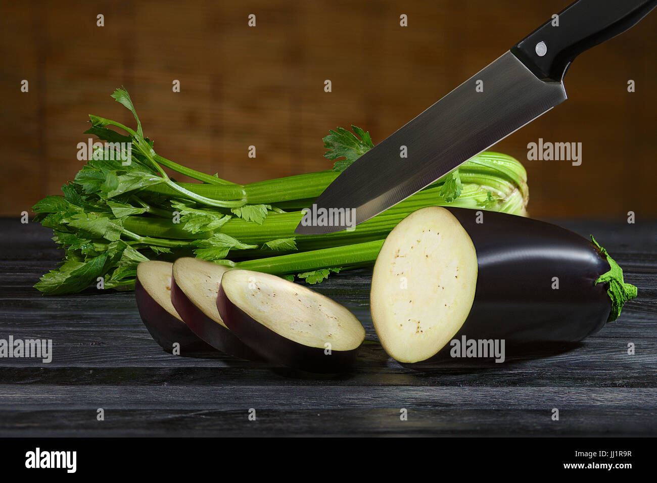 Couper les tranches d'aubergine de couteau et le céleri sur table en bois Banque D'Images