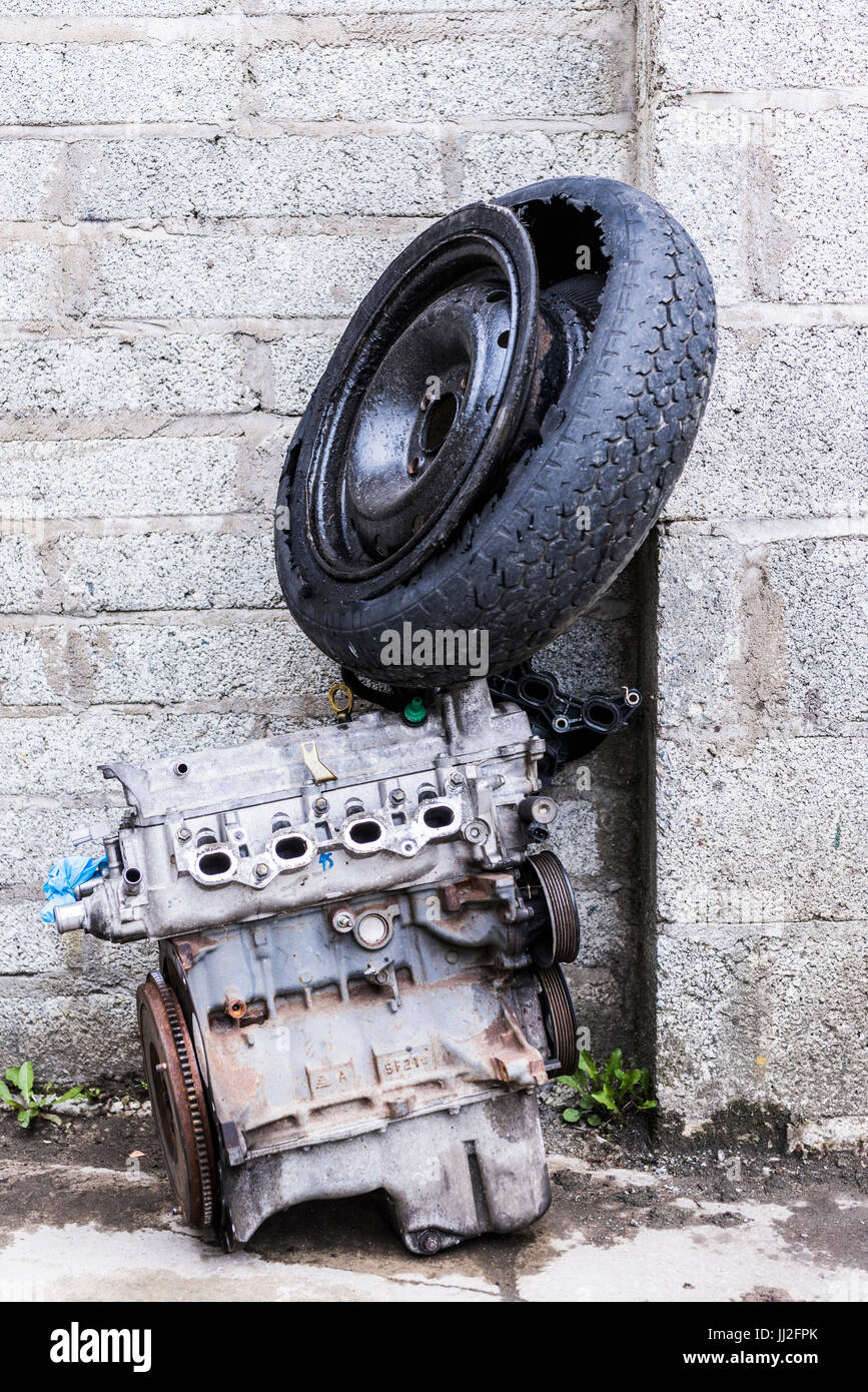 Ancien moteur et roue à pneu de voiture contre un dumping un vieux mur de blocs de Breeze. Banque D'Images