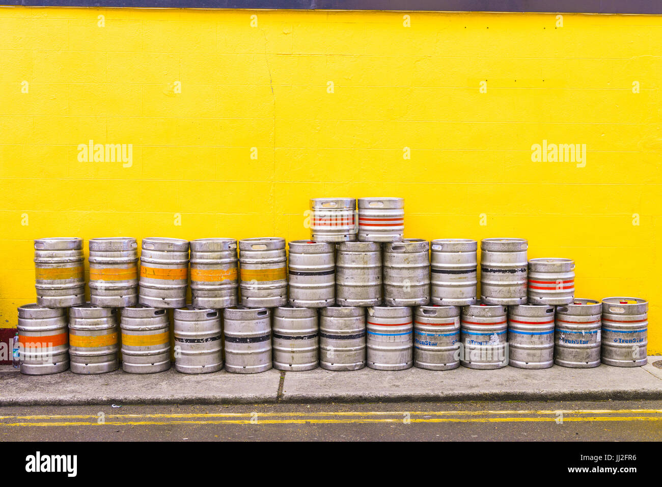 Les fûts de bière en aluminium empilés contre un mur orange peint à un pub irlandais. Banque D'Images