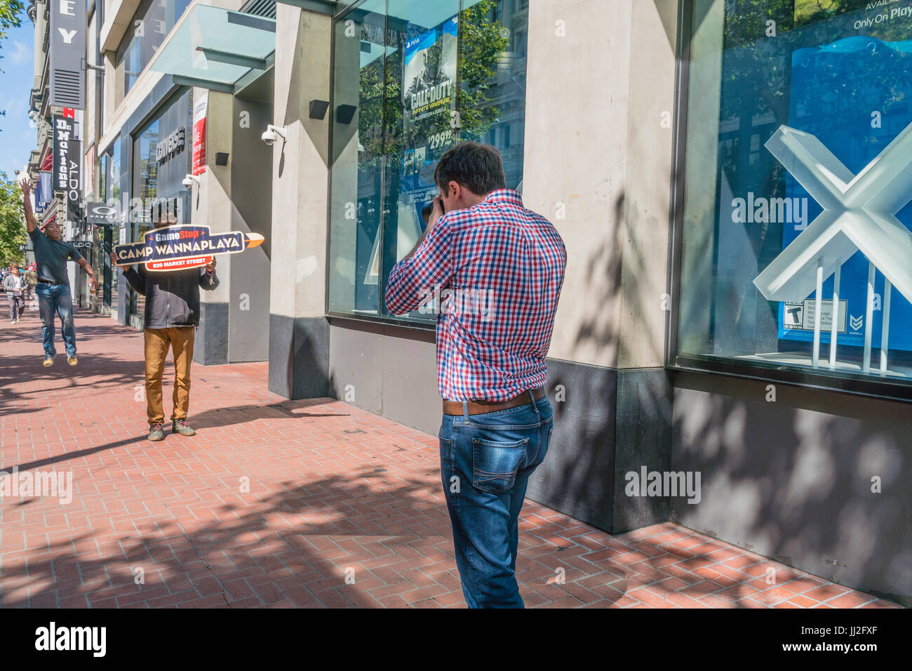 Un homme de race blanche tire une photographe afro-américain dont le travail est de transporter une pancarte pour Wannaplaya Camp autour de Market Street à San Fran Banque D'Images