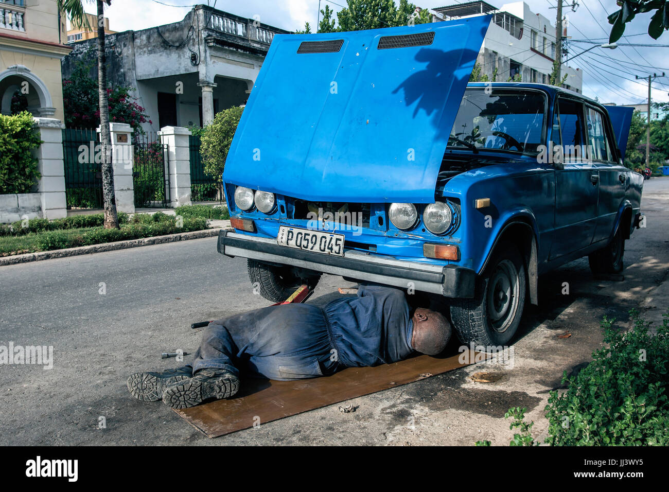 L'homme fixe une voiture d'époque le long d'une rue latérale à El Vedado, La Havane, Cuba Banque D'Images