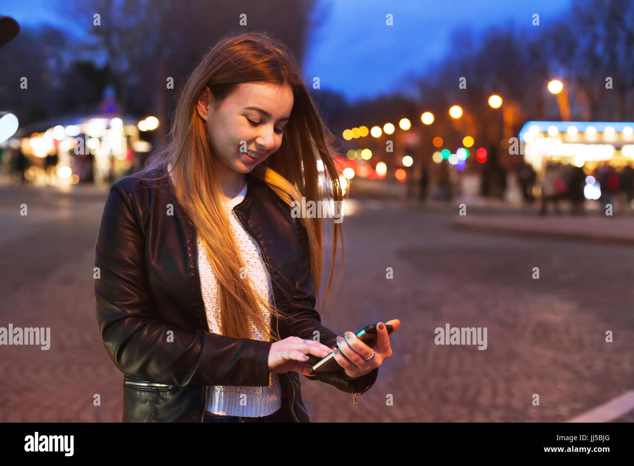 Jeune femme à l'aide du smartphone sur la rue par nuit et smiling Banque D'Images