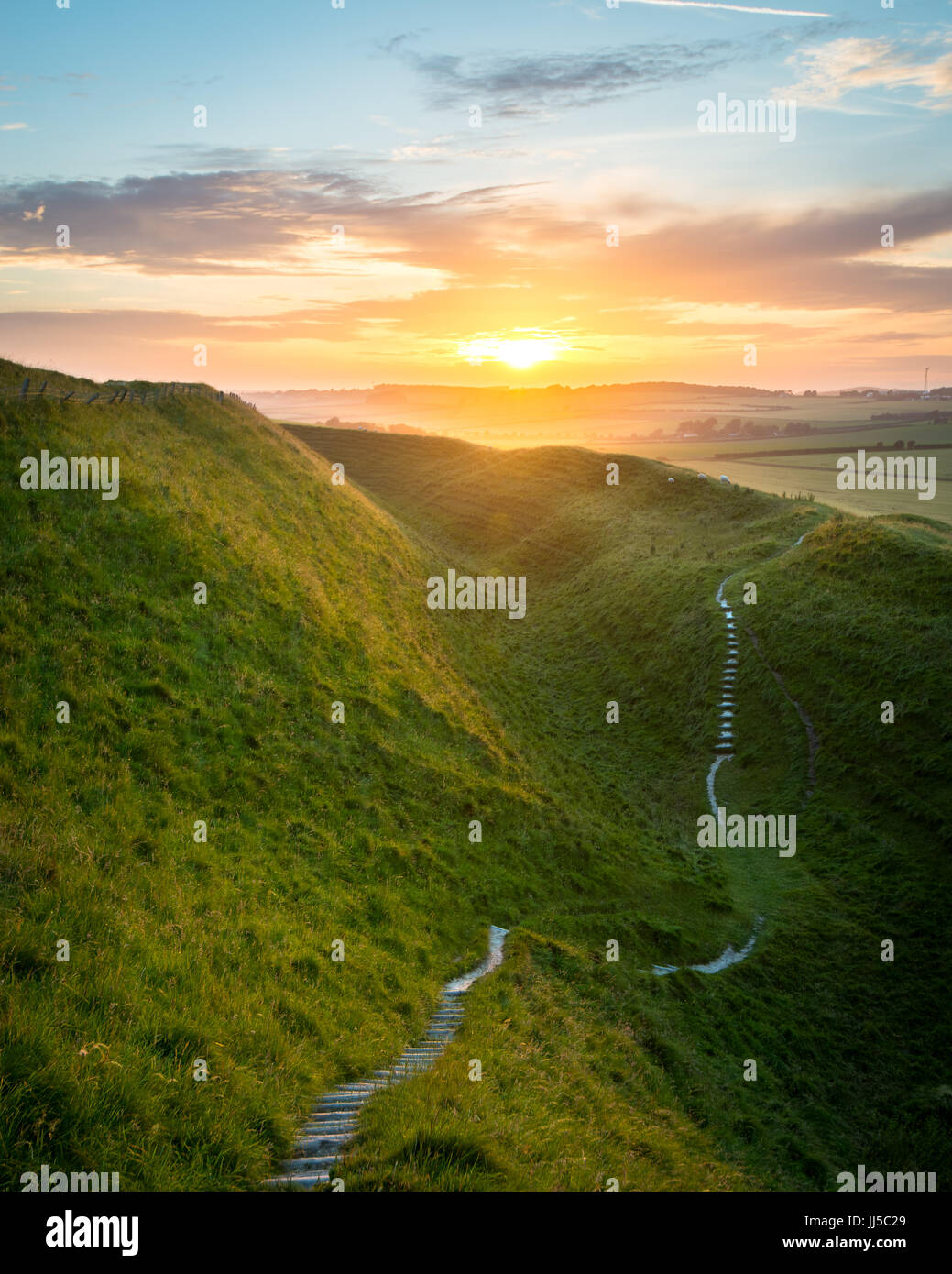Sentier serpente à travers les châteaux de jeune fille d'énormes remparts alors que le soleil se couchait au loin près de Dorchester, Dorset, UK Banque D'Images