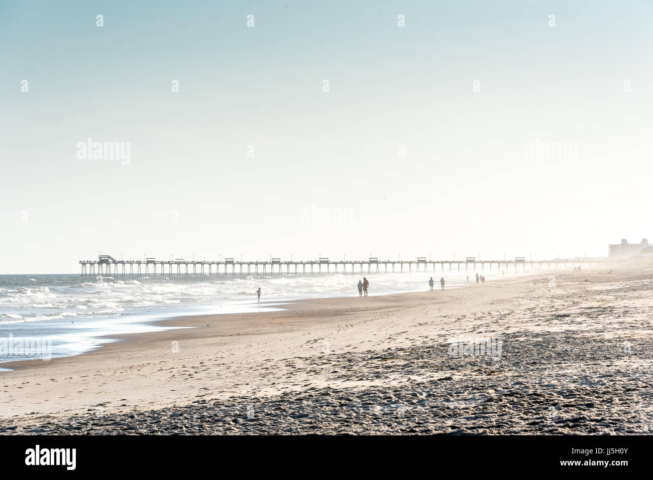 Les gens qui marchent sur l'île d'Emeraude beach w/ Bogue Pier à distance sur une plage, promenade du soir brumeux Crystal Coast de Caroline du nord, sud de l'Outer Banks Banque D'Images
