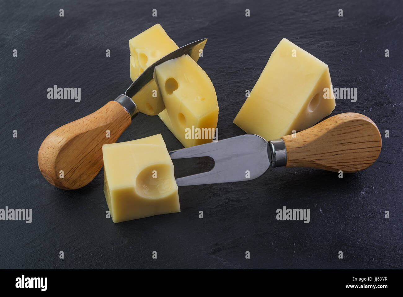 Trois morceaux de fromage sur une plaque d'ardoise noire avec fourchette et couteau Banque D'Images