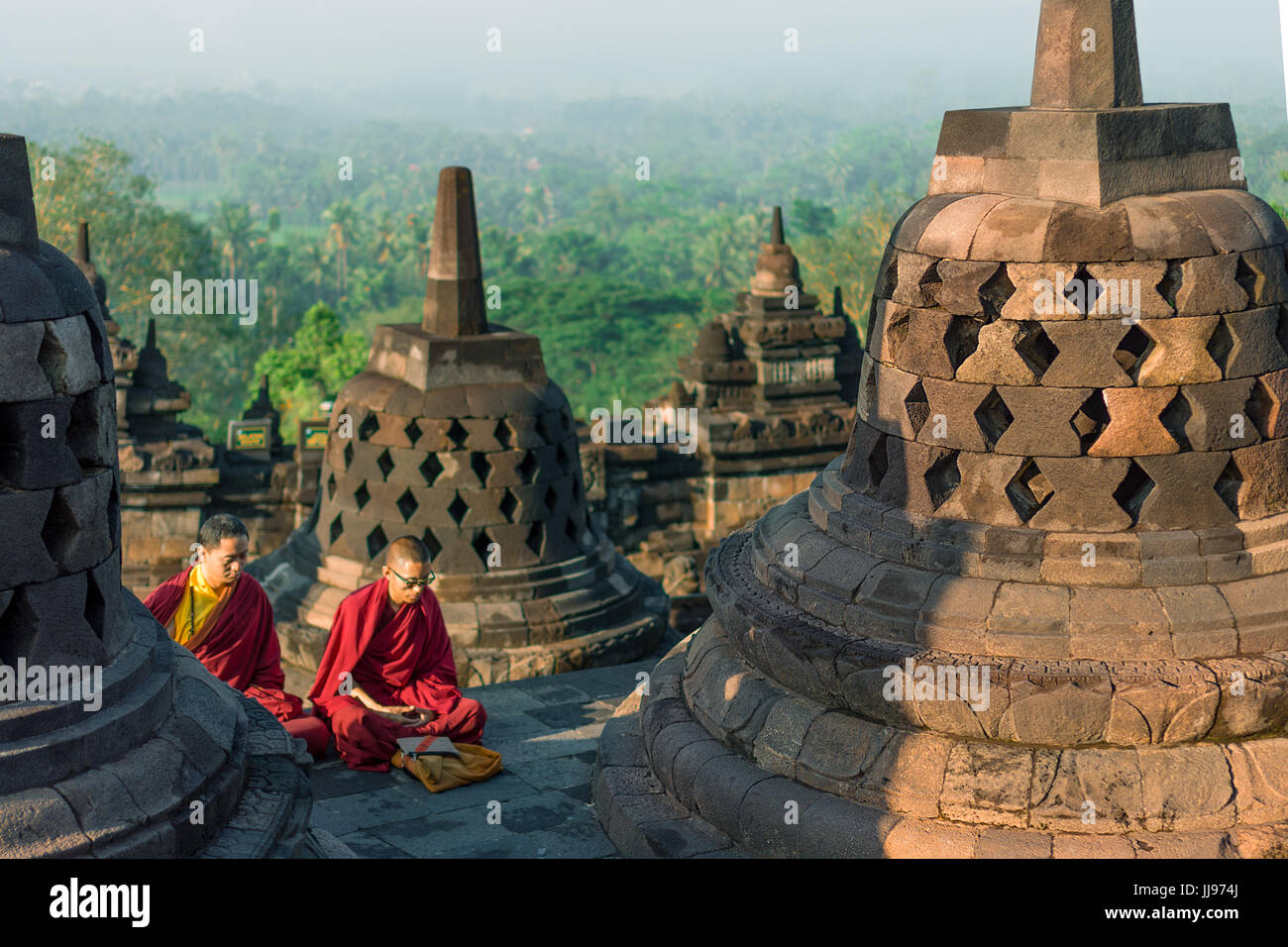 Robe rouge moines priant au lever du soleil sur le site du patrimoine mondial buddist temple Borobudur. Banque D'Images