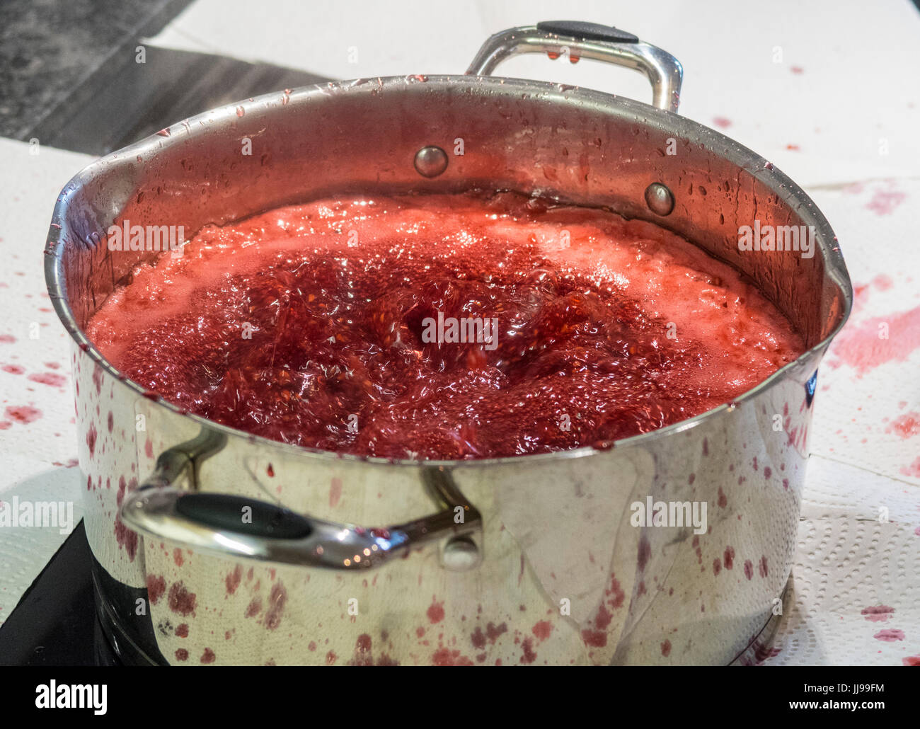 Confiture de framboises bouillante vigoureusement sur une plaque à induction dans un moule métallique, la région couverte de papier pour éviter les éclaboussures. Banque D'Images