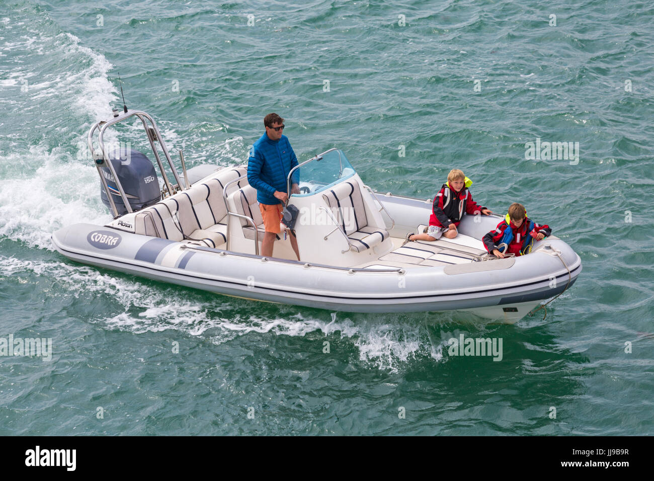 Homme et deux garçons dans Cobra Inflatable Boat boating dans le Solent entre Lymington et Yarmouth, Isle of Wight, Hampshire, Royaume-Uni en juillet Banque D'Images