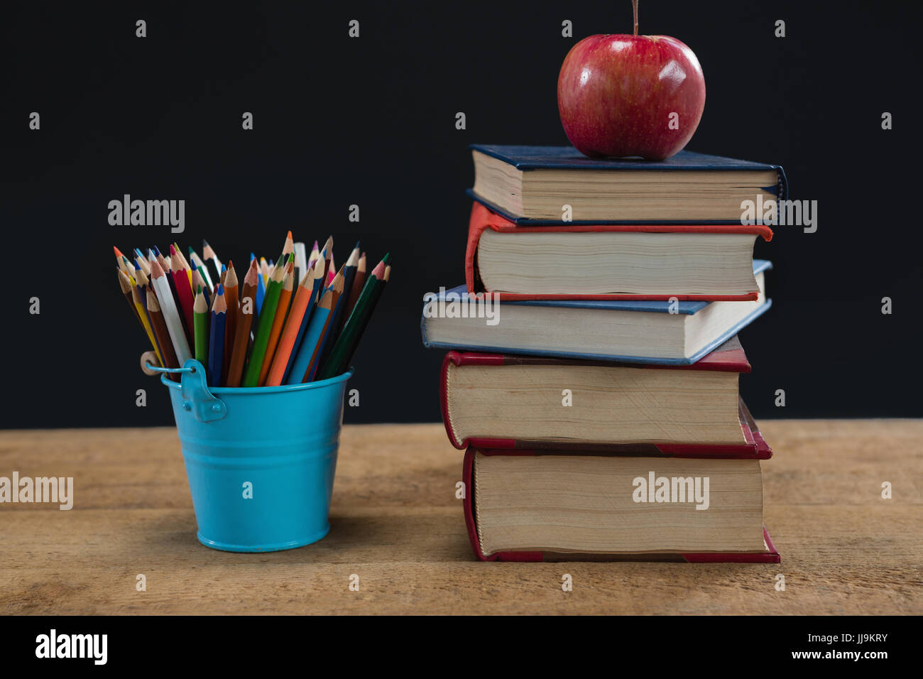 Apple sur la pile de livres avec des crayons de couleur sur le tableau sur fond noir Banque D'Images