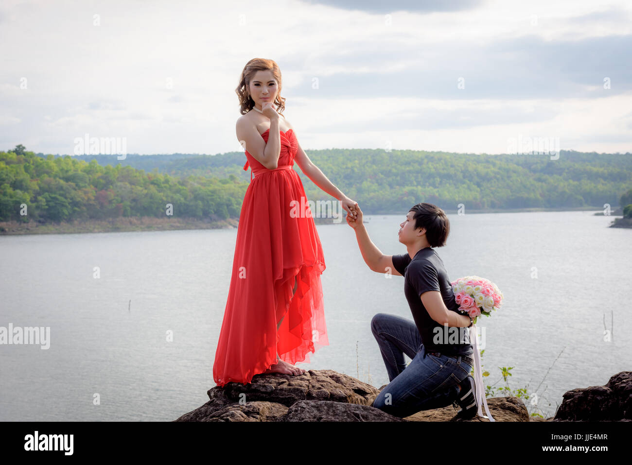 Jeune homme se cache un bouquet de fleurs derrière lui s'apprête à livrer une jeune femme en robe rouge. Banque D'Images