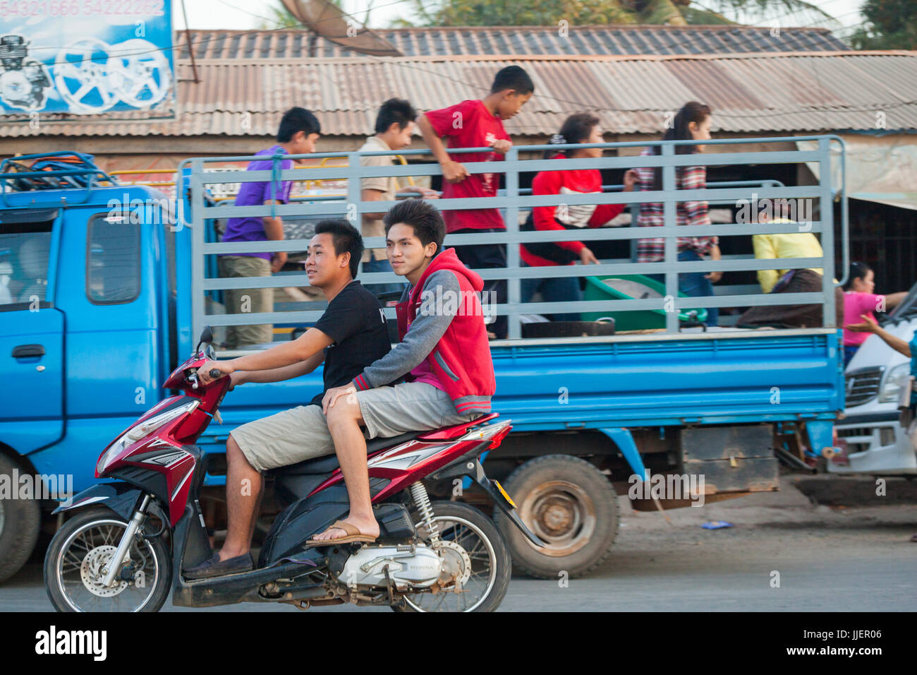 Les jeunes hommes se promener en trottinette passé ensemble en train de décharger un camion dans une rue animée de Luang Prabang, Laos. Banque D'Images