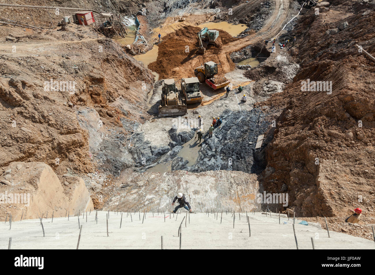 Un travailleur de la construction traverse un mur vertical en sautant sur armature en saillie au-dessus de travaux d'excavation sur le site de construction du barrage de # 5 sur la rivière Nam Ou au Laos. Banque D'Images