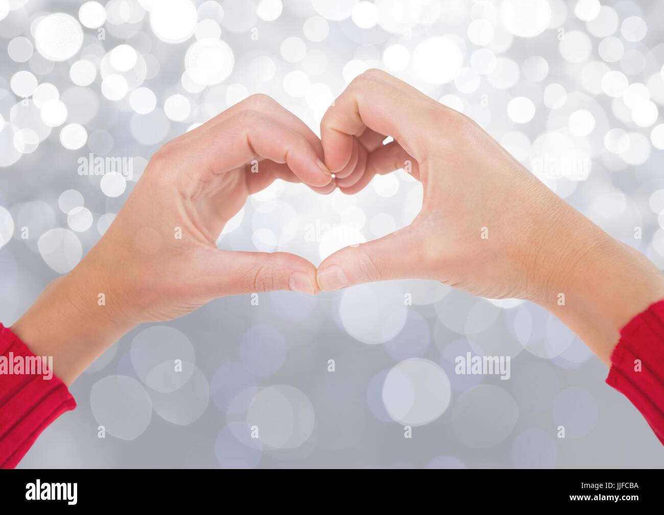 Digital composite des mains en forme de coeur avec l'arrière-plan flou léger pétillant Banque D'Images