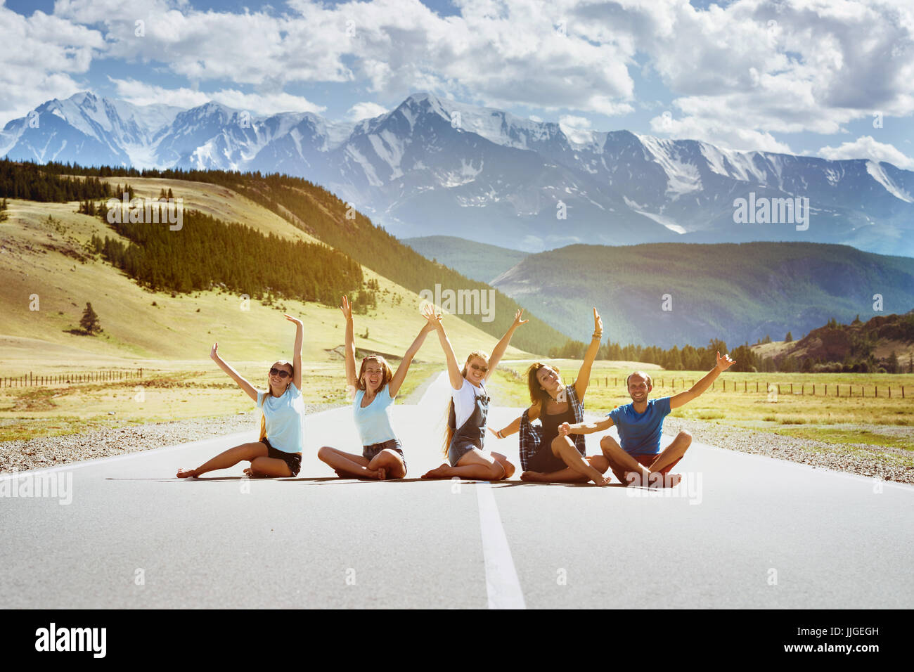 Groupe de cinq amis s'amusant heureux assis sur la route droite sur fond de montagnes. Concept d'amitié ou de l'équipe Banque D'Images