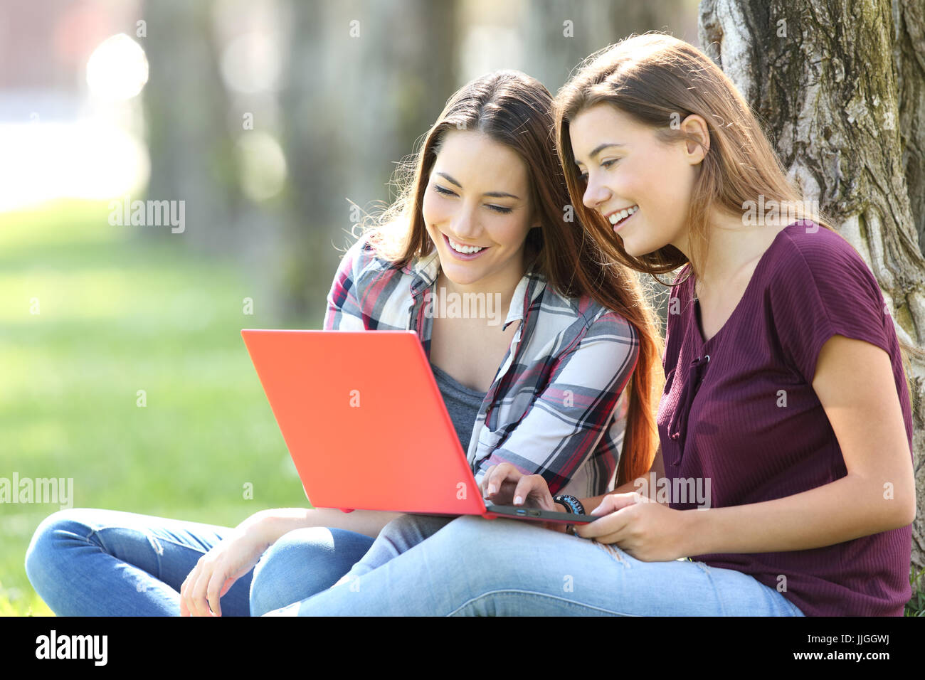 Deux professionnels de la recherche d'amis en ligne de contenu multimédia dans un ordinateur portable rouge assis sur l'herbe dans un parc Banque D'Images