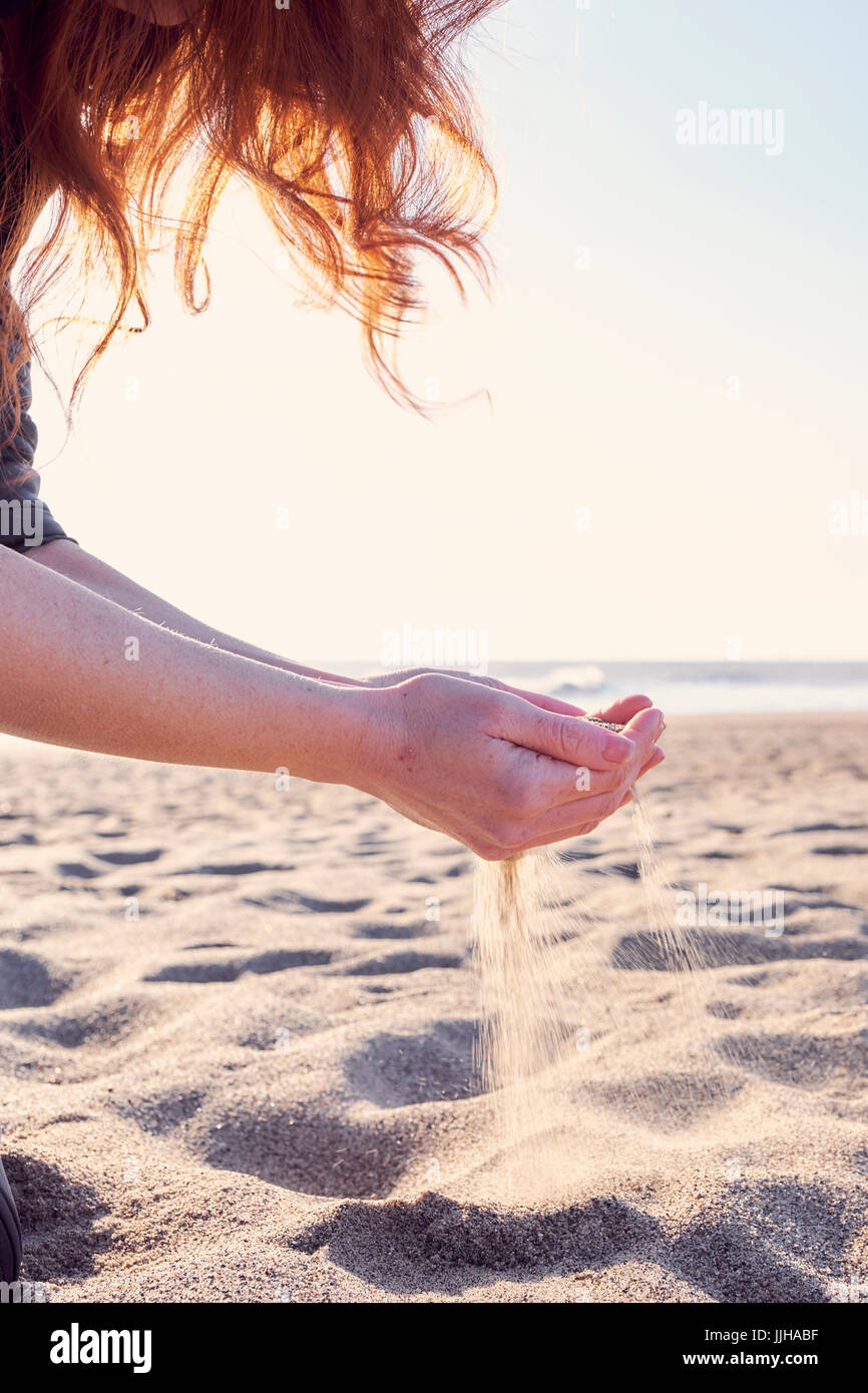 Une jeune femme tamisant le sable par ses mains sur la plage. Banque D'Images