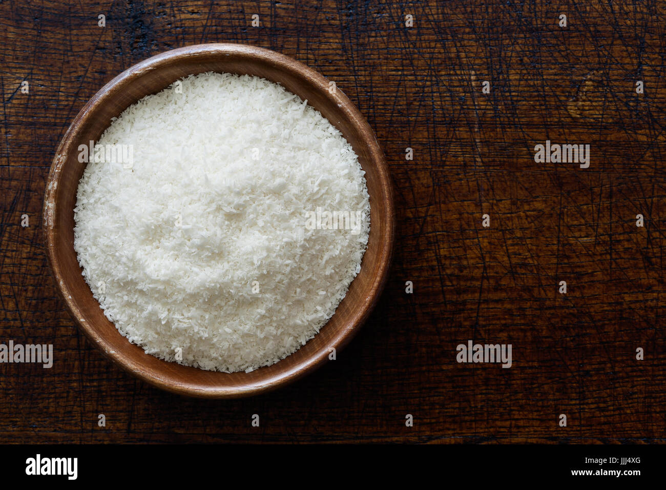 Noix de coco desséchée dans le noir bol en bois isolé sur bois marron foncé à partir de ci-dessus. Banque D'Images
