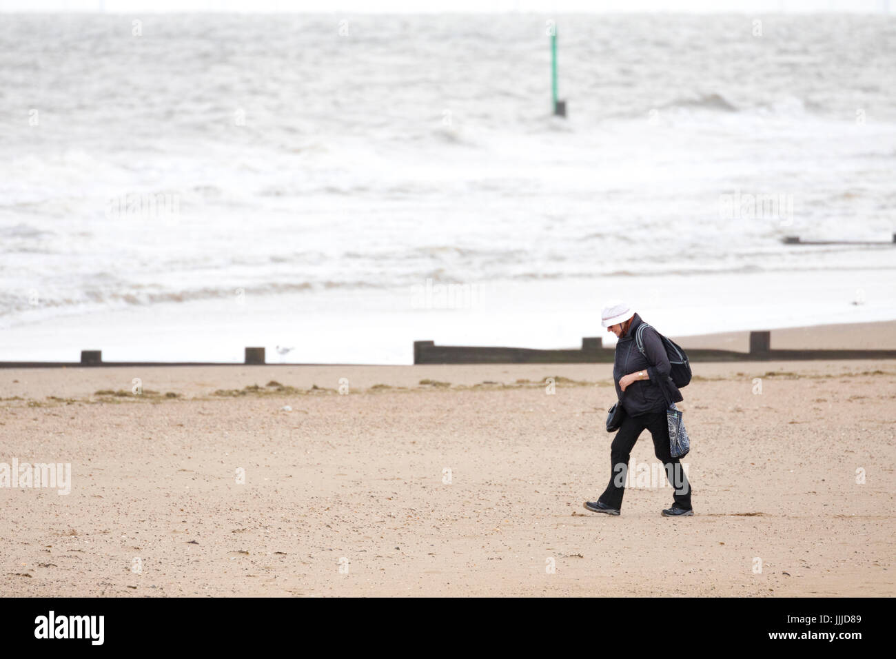 Une seule femme habillé pour l'hiver, mais sur un jour pluvieux et venteux sur la plage de Muro, Denbighshire, Wales, UK Banque D'Images