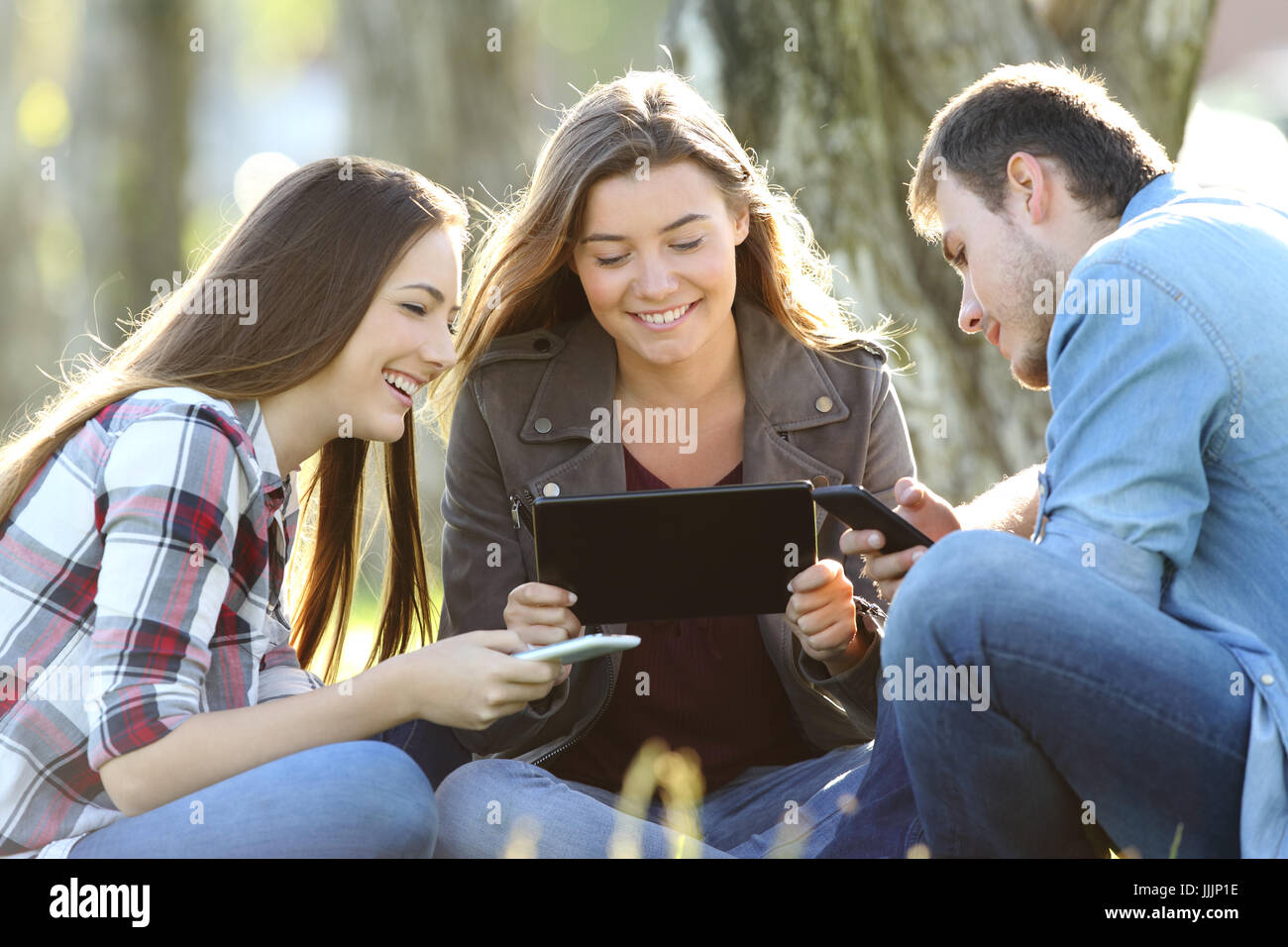 Trois amis à l'aide de plusieurs appareils à l'extérieur assis à l'extérieur dans un parc Banque D'Images