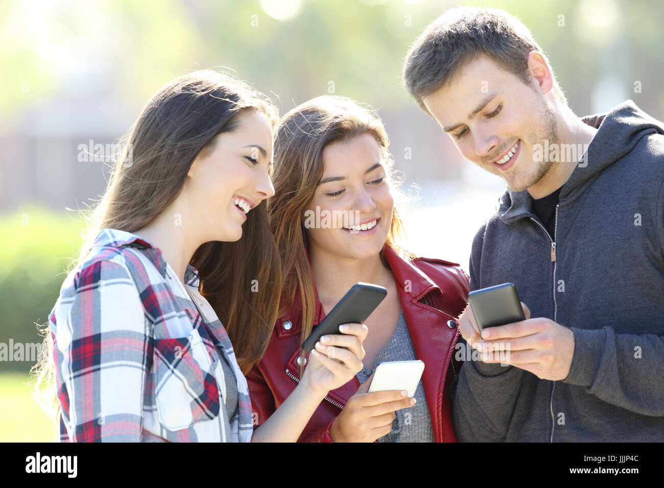 Happy teen trois amis qui partagent des smart phone content en plein air Banque D'Images