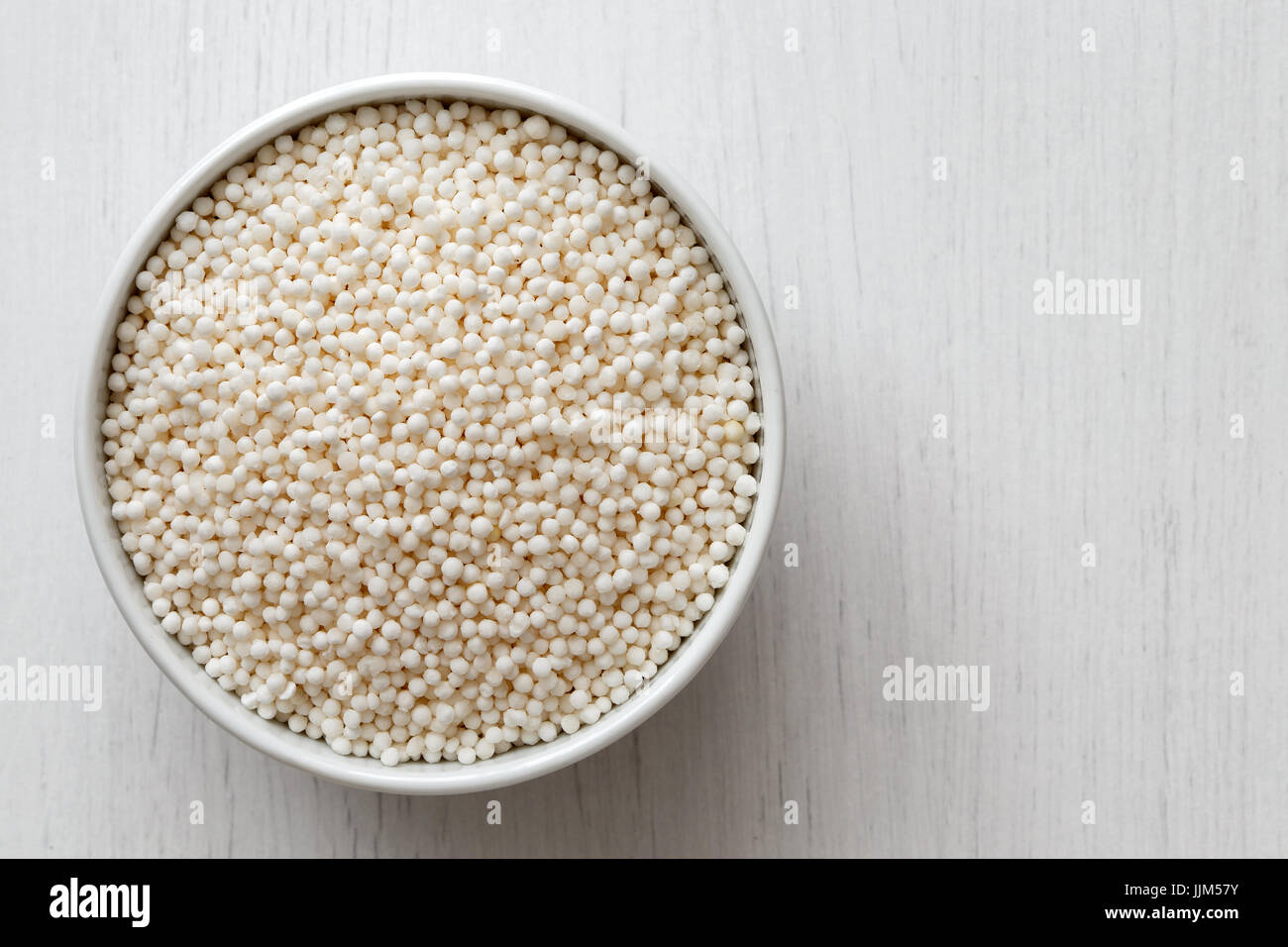 Perles de tapioca sec dans Bol en céramique blanc isolé sur bois peint en blanc à partir de ci-dessus. Banque D'Images