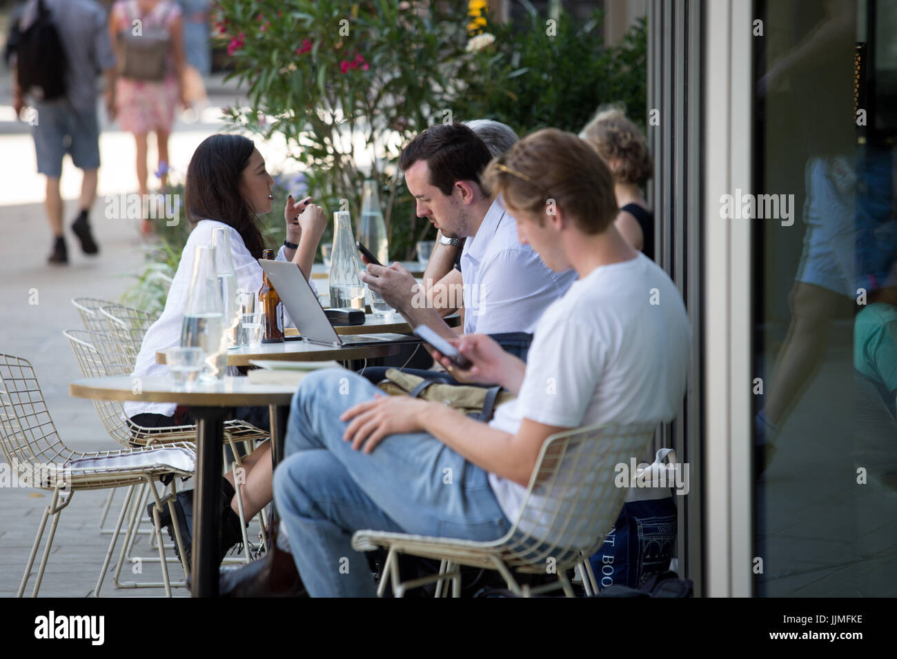 Les gens assis à l'extérieur d'un café à parler, à l'aide de téléphones portables et les ordinateurs portables. Prises autour de grenier Square, Kings Cross, London Banque D'Images