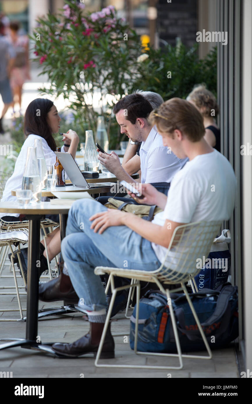 Les gens assis à l'extérieur d'un café à parler, à l'aide de téléphones portables et les ordinateurs portables. Prises autour de grenier Square, Kings Cross, London Banque D'Images