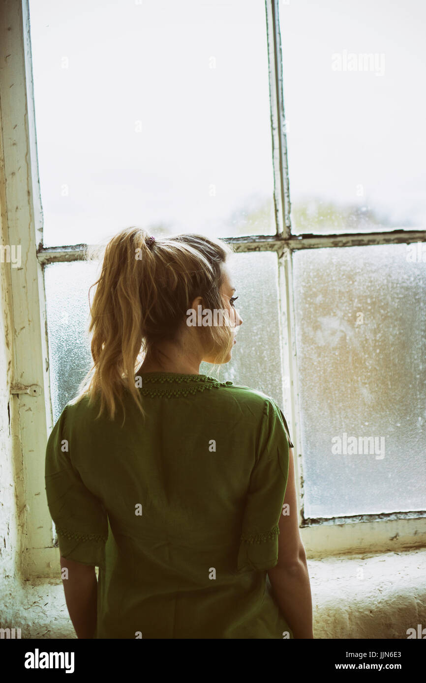 Vue arrière d'une jeune femme blonde debout près de la fenêtre Banque D'Images
