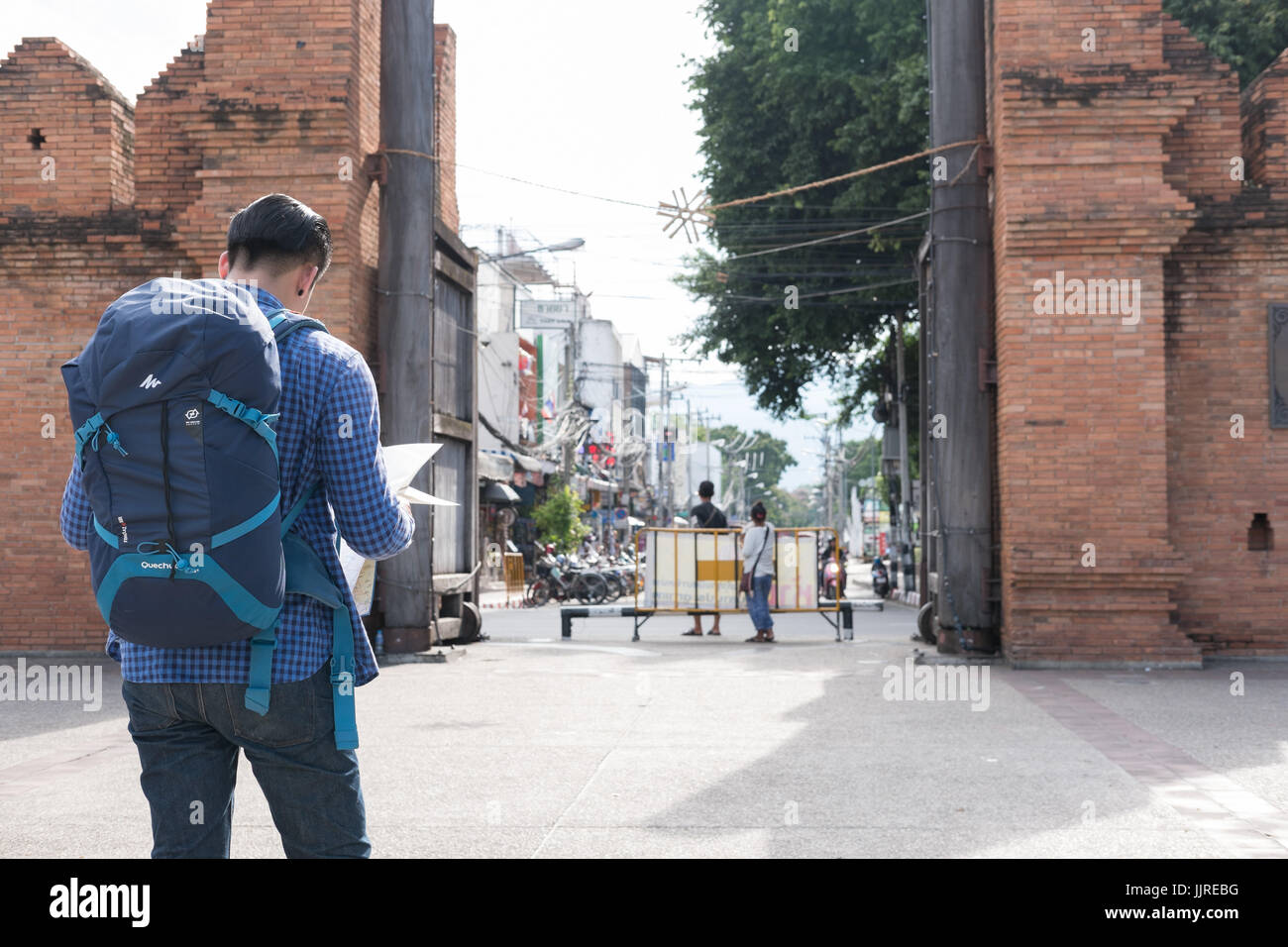 Chiang Mai, Thaïlande - 29 juin 2017 : young asian man wearing blue jeans et blouson reading map debout près de l'ancien mur de briques orange sac avec Banque D'Images