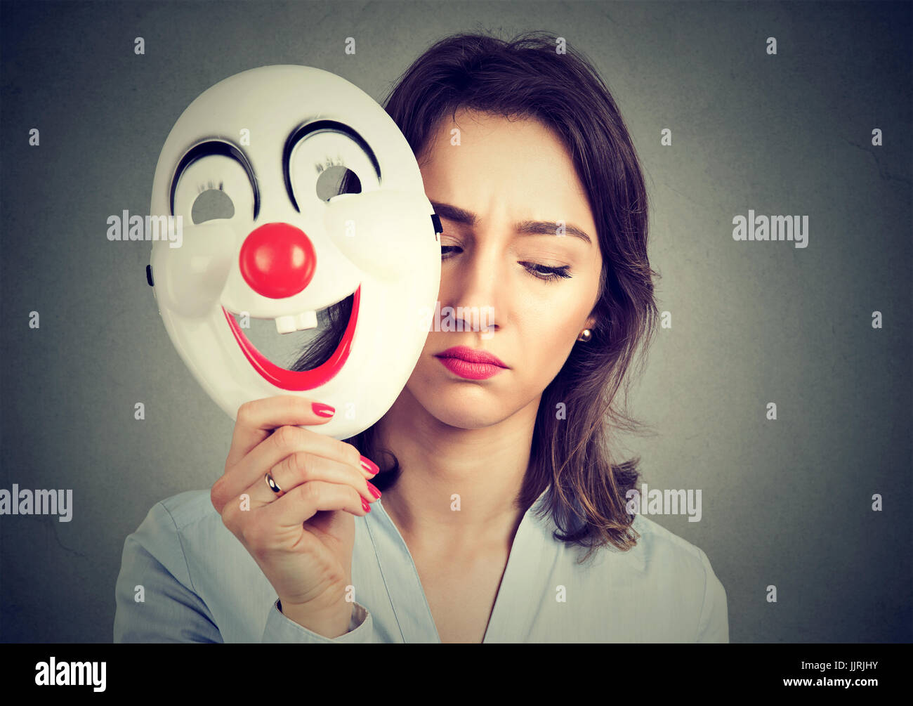 Triste Portrait woman taking off masque clown heureux isolé sur fond de mur gris. Les émotions humaines sentiments Banque D'Images