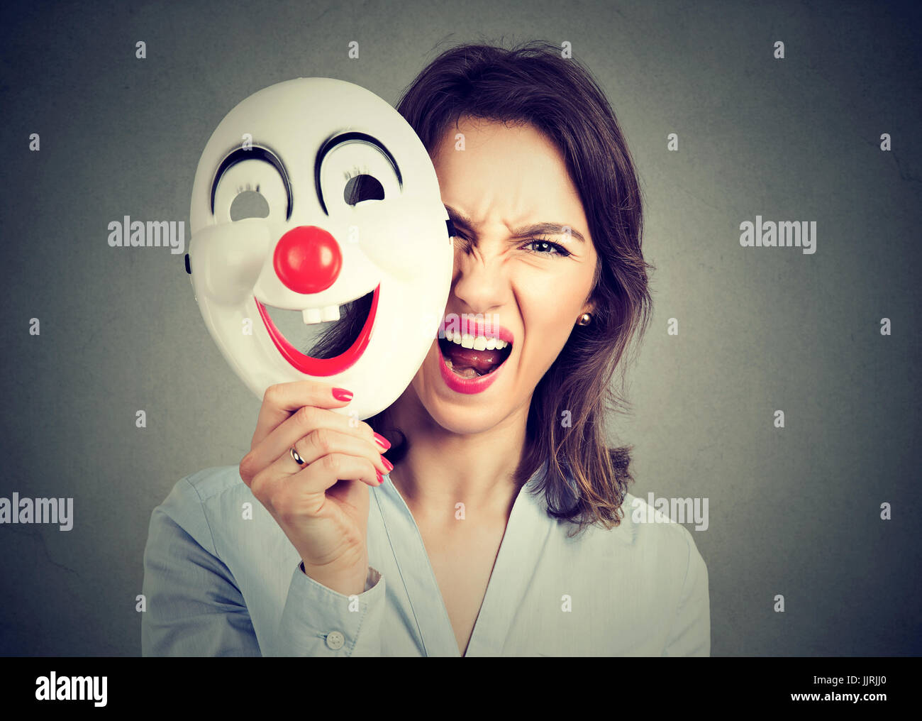Hurlant de colère Portrait woman taking off masque clown heureux isolé sur fond de mur gris. Les émotions humaines sentiments négatifs Banque D'Images
