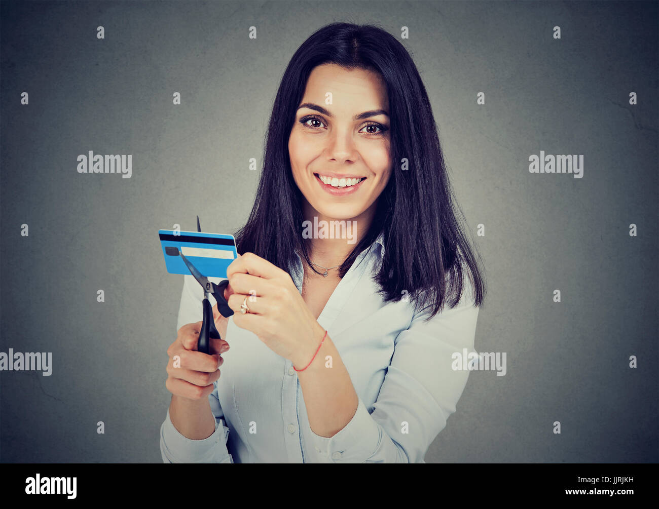 Happy woman réduire de moitié sa carte de crédit avec des ciseaux isolé sur fond gris Banque D'Images