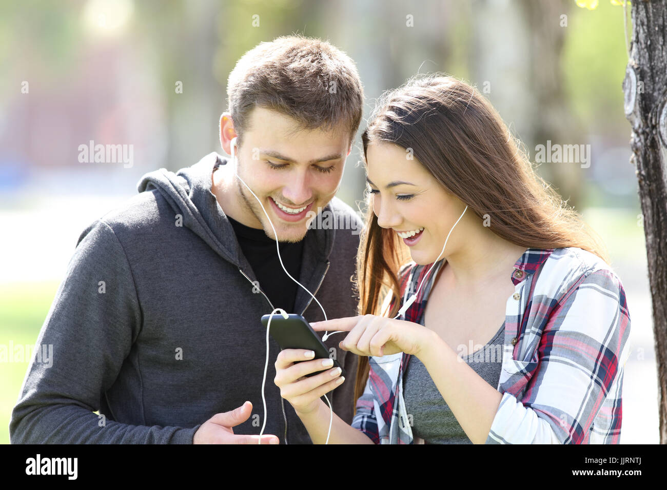 Deux amis à l'écoute de la musique ensemble et la sélection de chansons dans un smart phone outdoors Banque D'Images