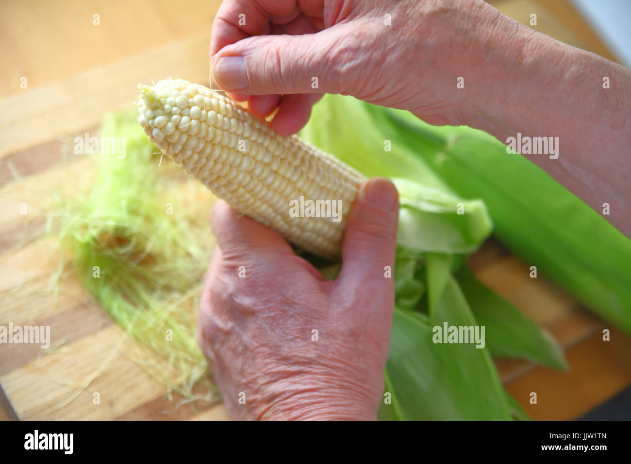 Homme plus âgé de la dépose de la soie de maïs de l'épi de maïs blanc Banque D'Images