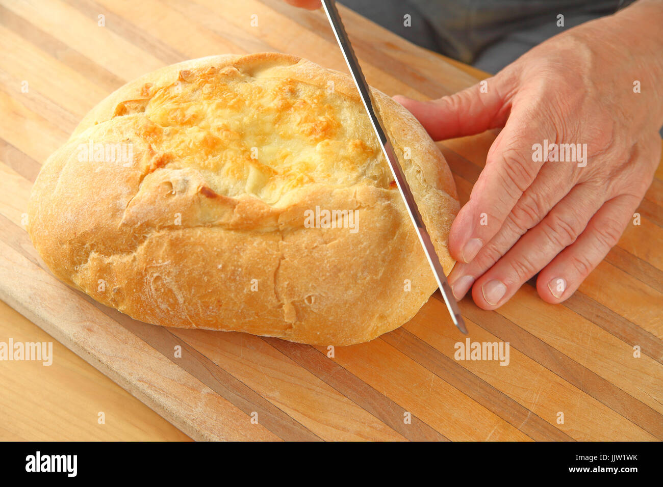 Un homme commence à couper les coupes d'une miche de pain au fromage artisanal Banque D'Images