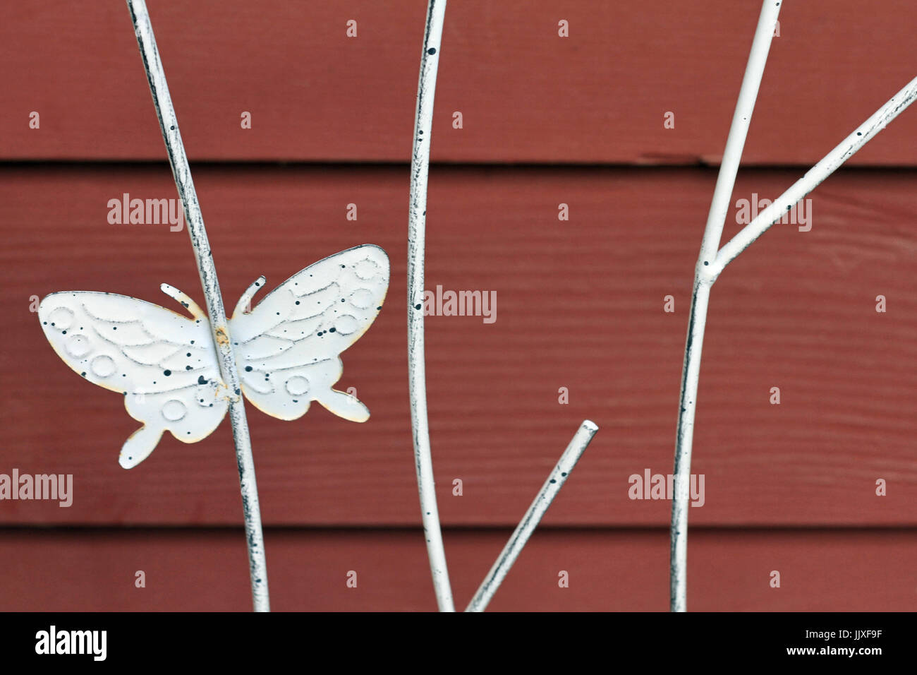 Un métal blanc papillon sur un treillis de plantes flotte sur un fond de bois noir. Banque D'Images