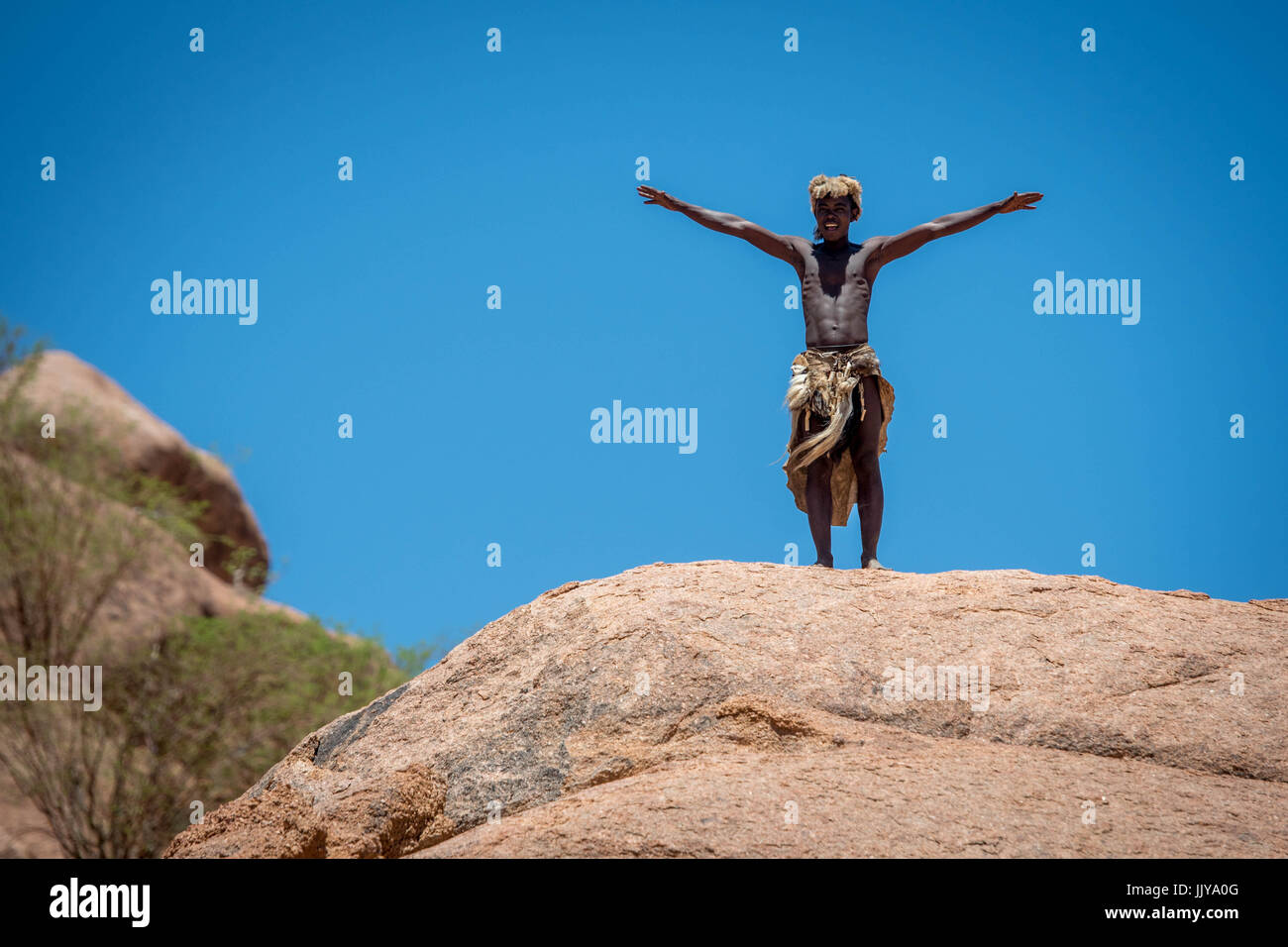 Au Damara musée vivant, un membre de la tribu des hommes se dresse au sommet d'un gros rocher avec ses bras tendus. Le Musée vivant est situé au nord de Twyfe Banque D'Images