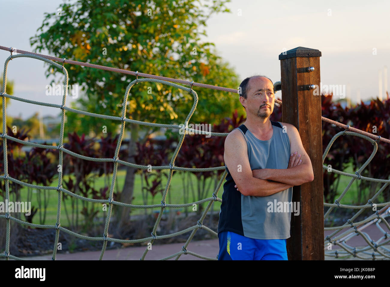 Homme de race mixte debout les bras croisés au coucher du soleil dans un parc Banque D'Images