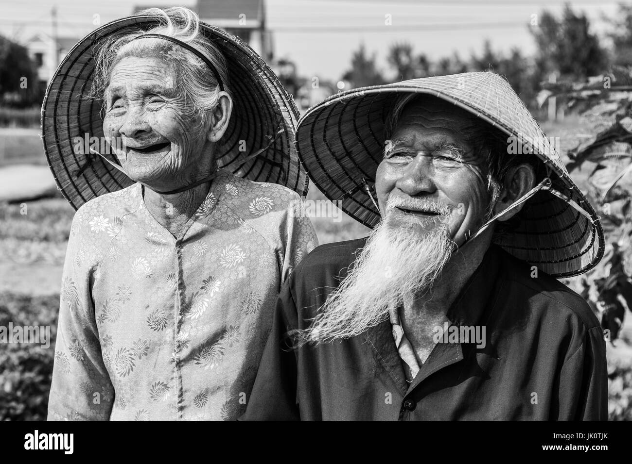 Vieux couple Smiling vietnamiens en tenue traditionnelle et chapeaux coniques en noir et blanc Banque D'Images