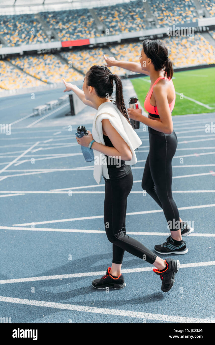 Les sportives jeunes fatigués avec des bouteilles d'eau de marcher sur une piste de course stadium Banque D'Images