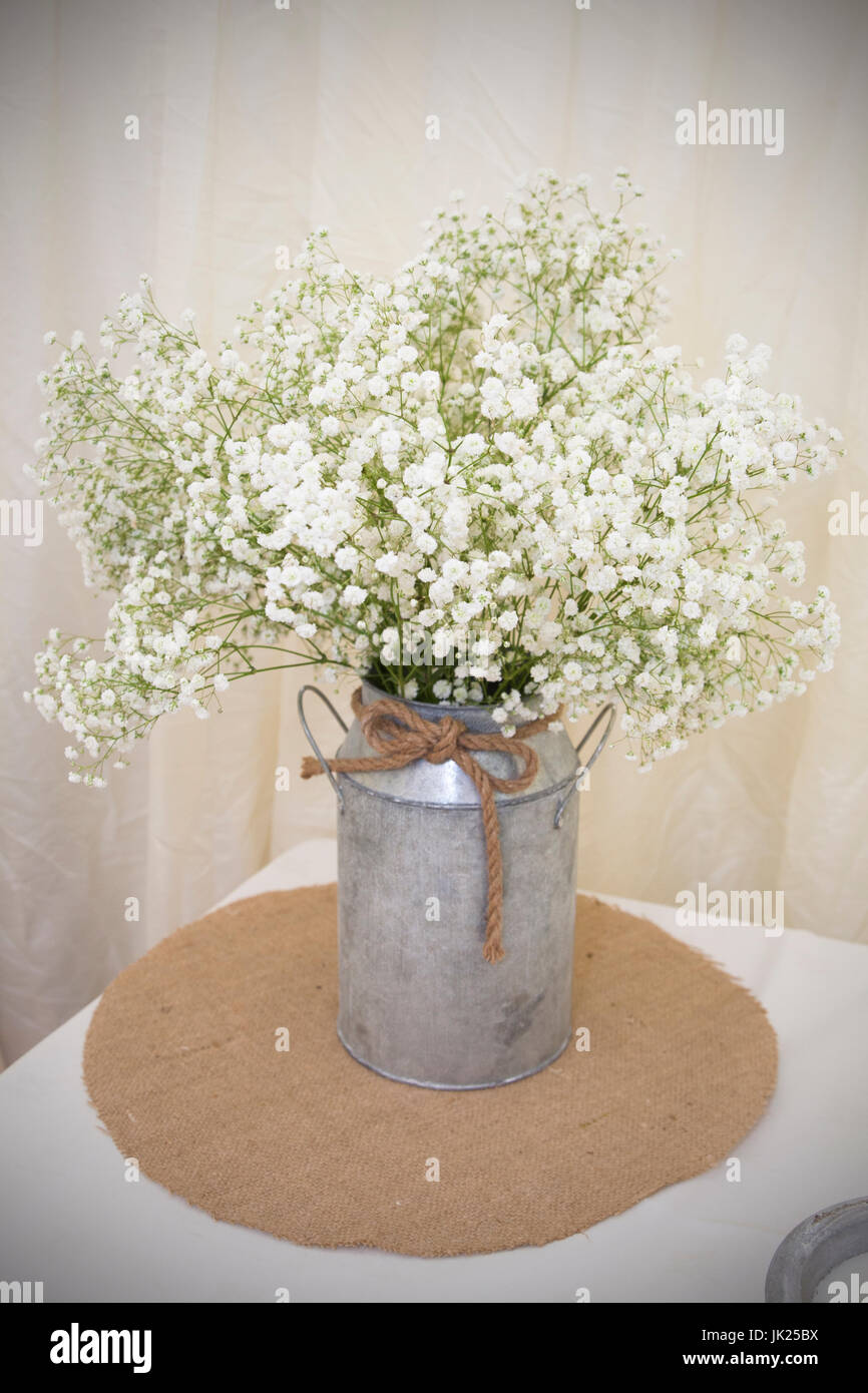 La respiration du bébé blanc Bouquet situé dans une baratte métallique avec corde rustique pour la décoration. Placé sur un hessiam matt tissu sur une nappe blanche. Banque D'Images