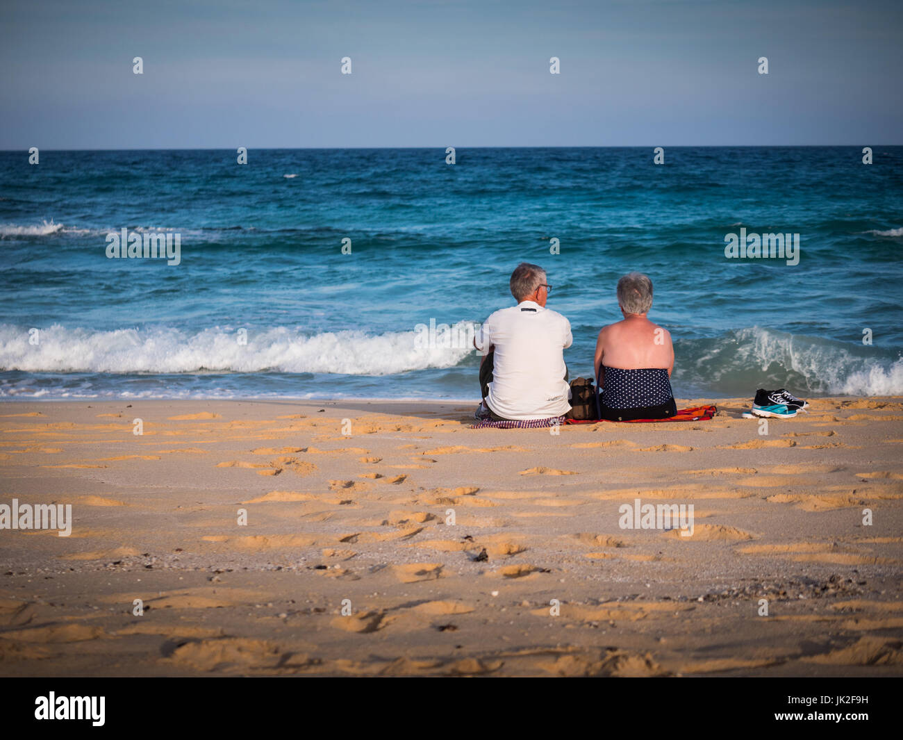 Un couple assis sur une plage de sable fin et regardez vers la mer, des vagues briser près de leurs pieds Banque D'Images