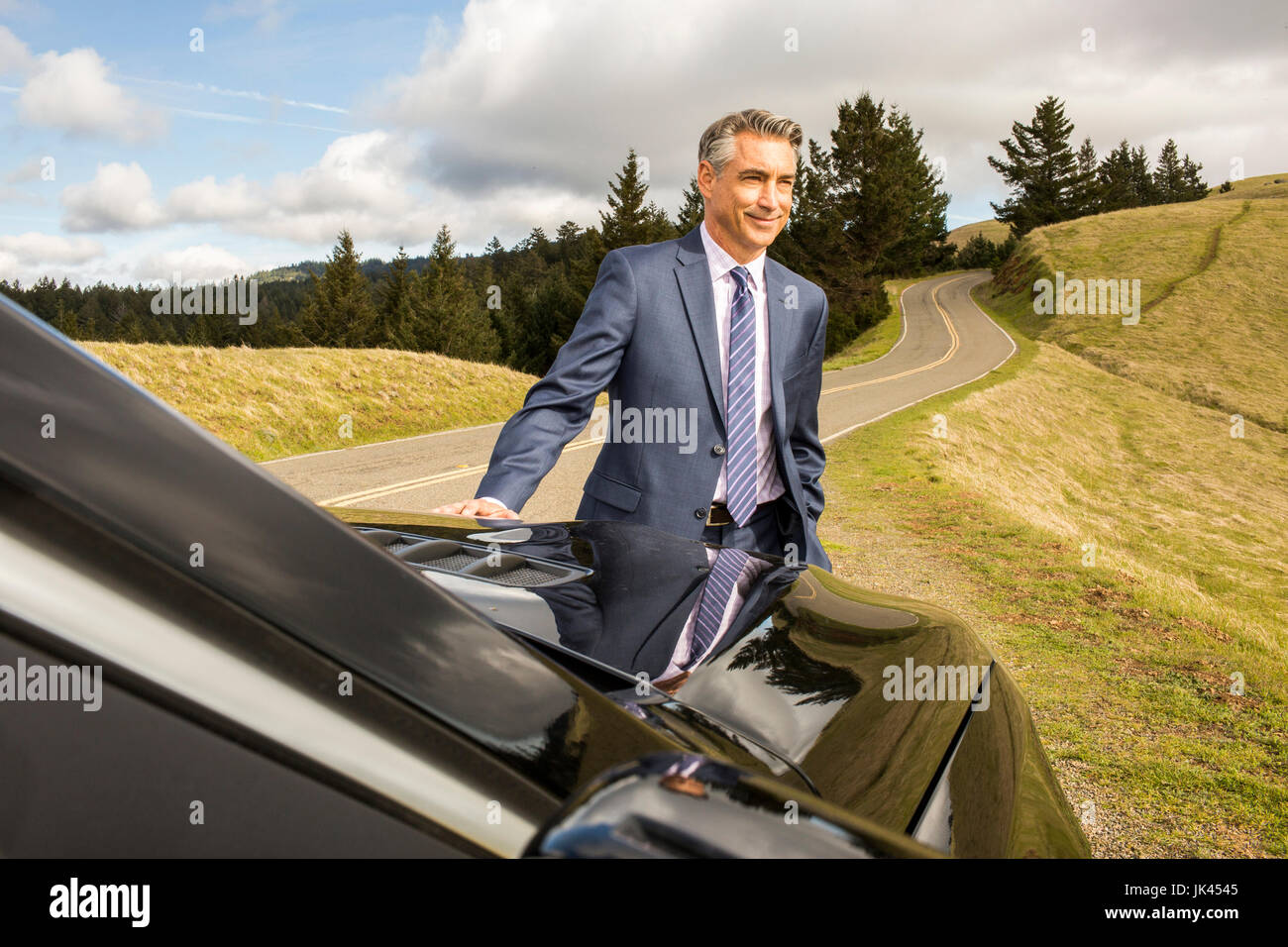 Smiling Caucasian businessman leaning on car Banque D'Images