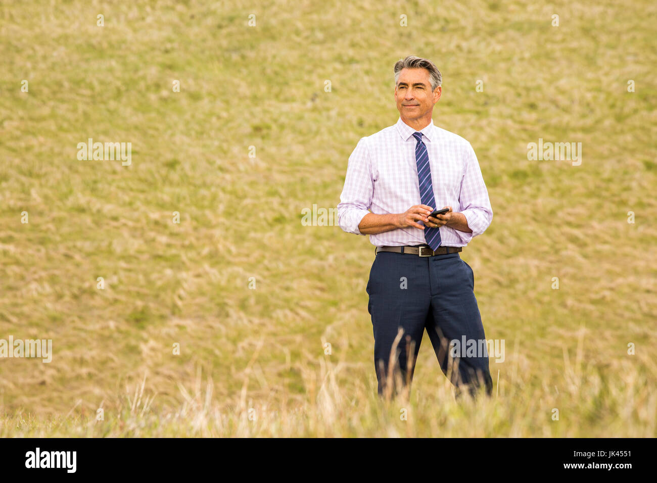 Caucasian businessman standing in grass holding cell phone Banque D'Images