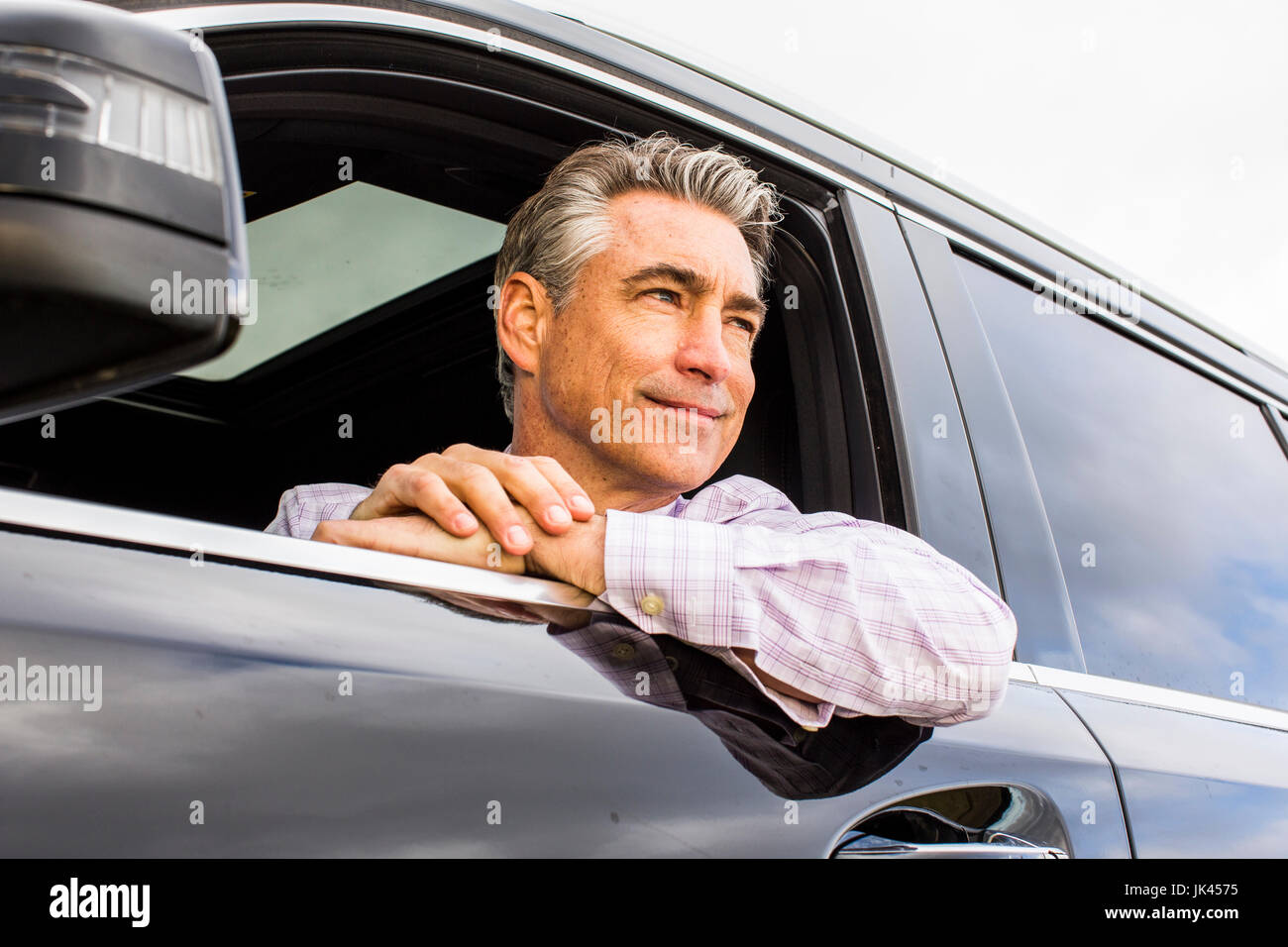 Smiling Caucasian businessman leaning on car window Banque D'Images