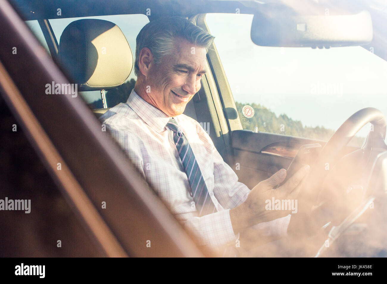 Smiling Caucasian businessman sitting in car texting on cell phone Banque D'Images