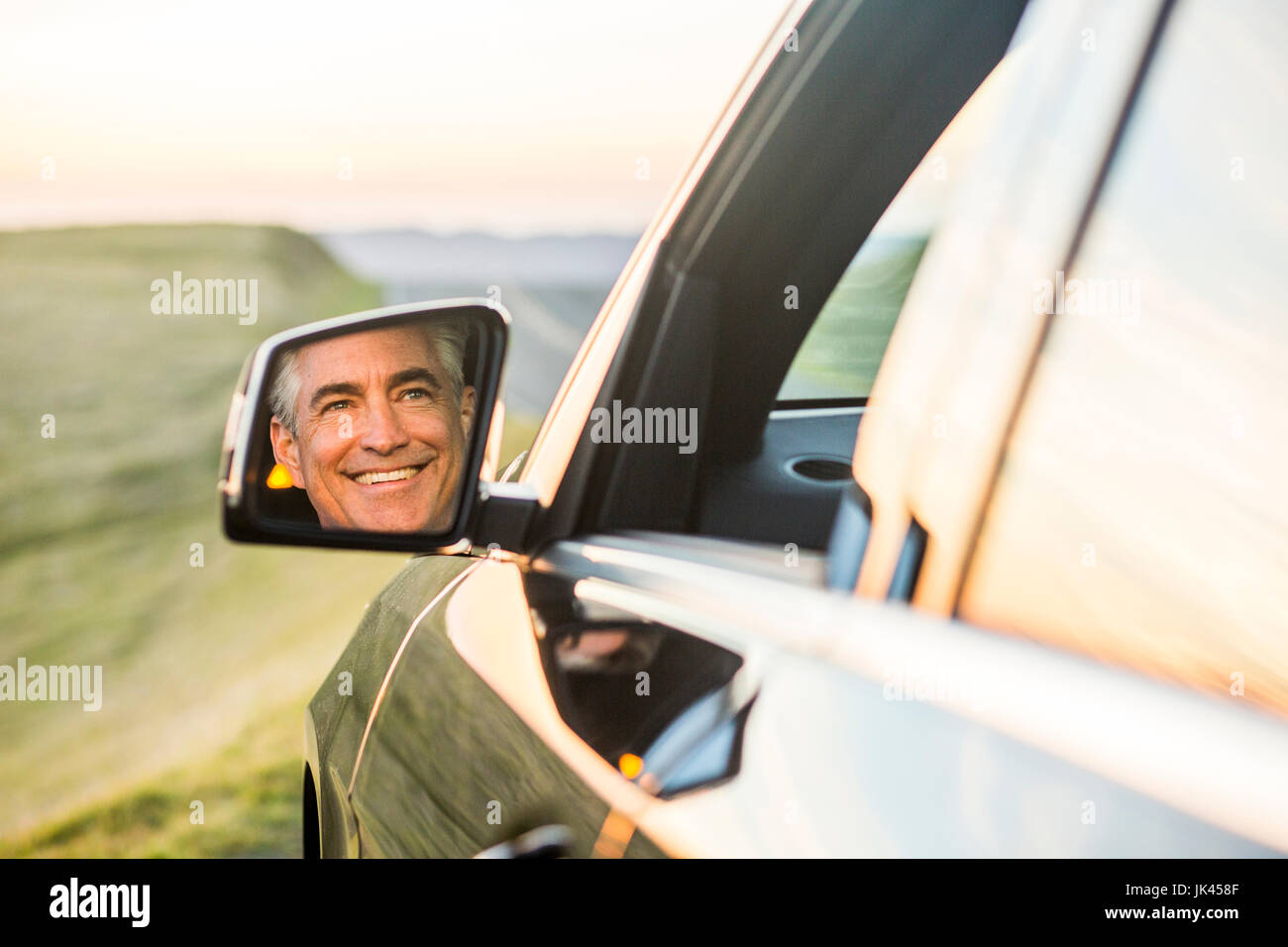 Reflet dans le miroir de smiling Caucasian man driving car Banque D'Images