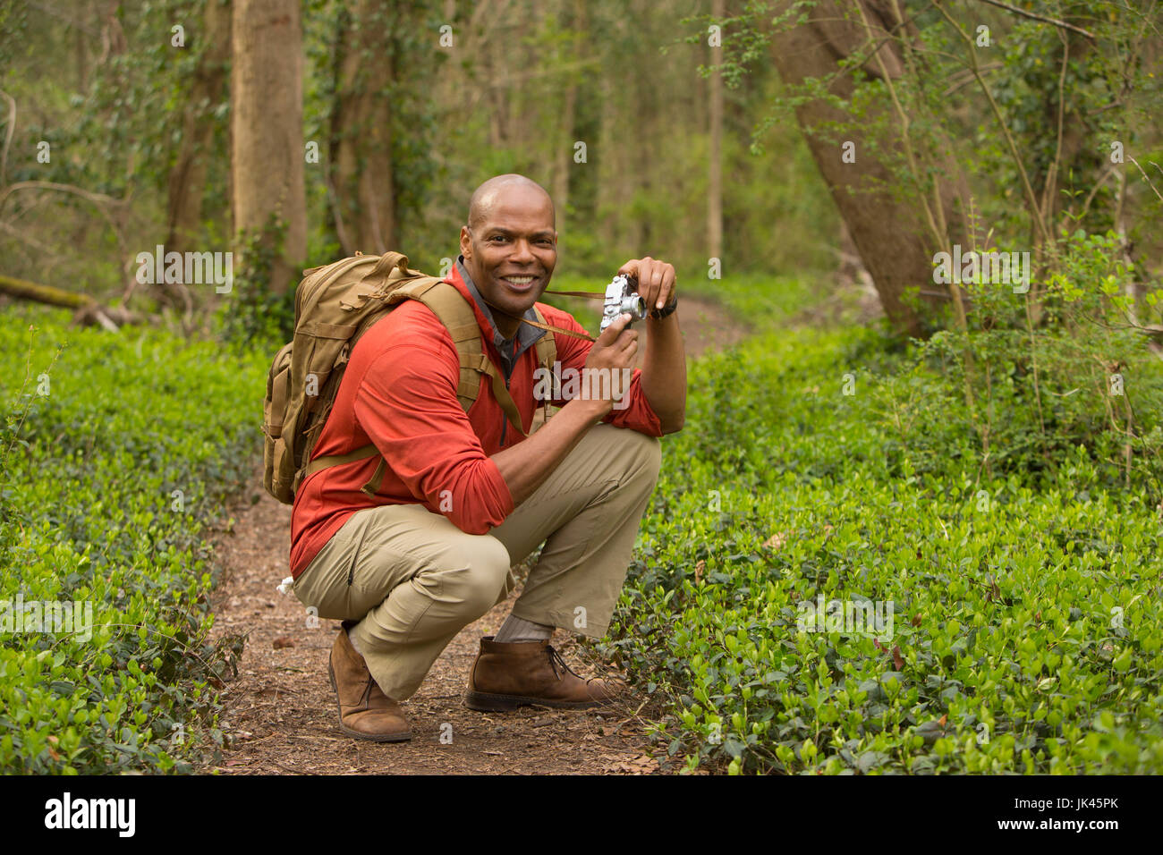 African American man crouching on path in forest holding camera Banque D'Images