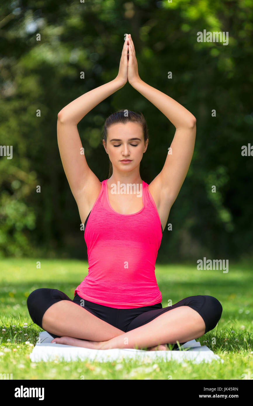 Jeune femme en bonne santé fit femme ou fille pratiquant le yoga poser sur un tapis à l'extérieur dans un parc naturel de l'environnement verdoyant et tranquille Banque D'Images